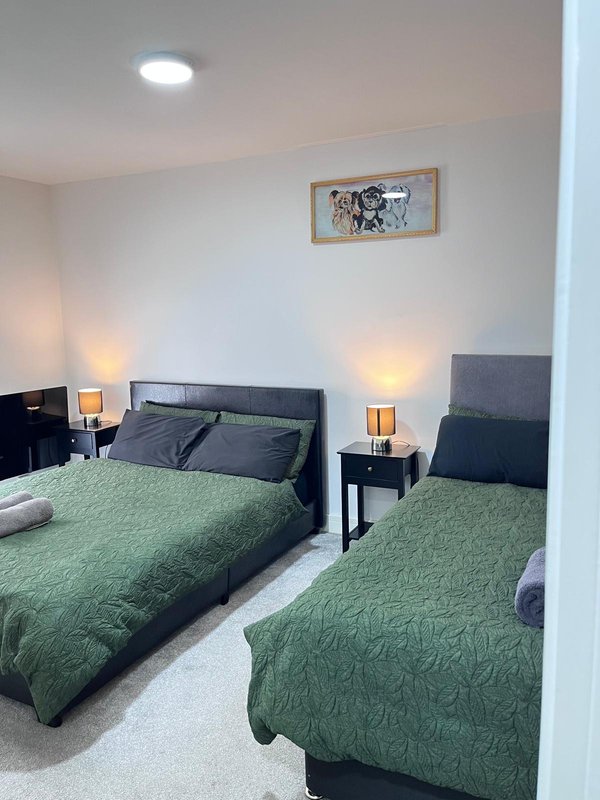 Bedroom with two beds, green quilted bedding, black headboards, bedside tables with lamps