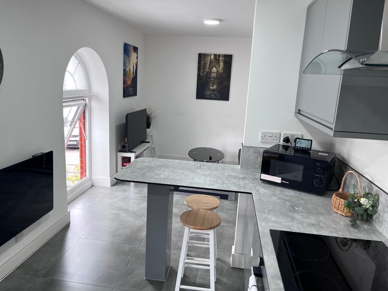 Modern kitchen with grey marble island, white cabinetry, black appliances and arched doorway