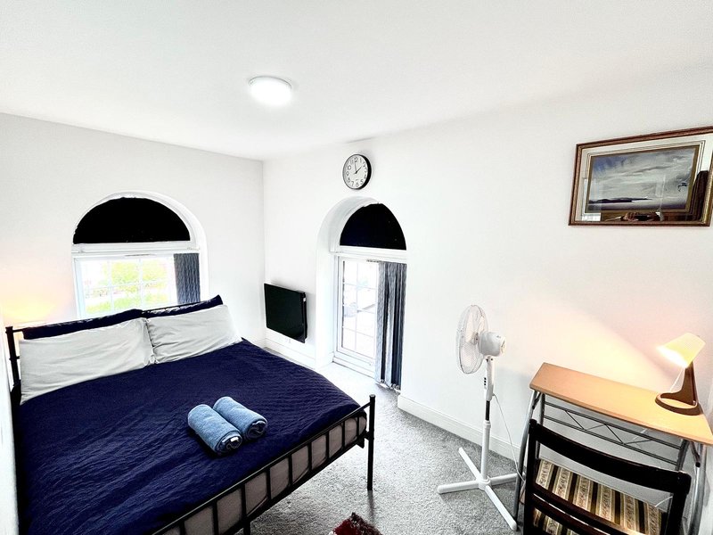 Bedroom with double bed, navy bedding, arched windows, wall clock, and desk lamp