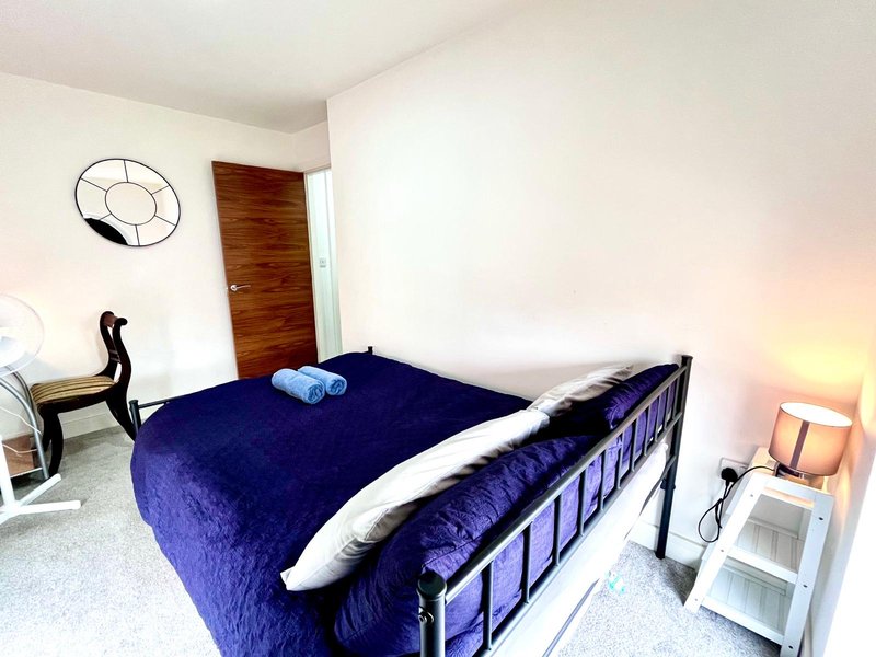 Bedroom with single metal-frame bed, blue bedding, wooden door, wall clock and desk chair