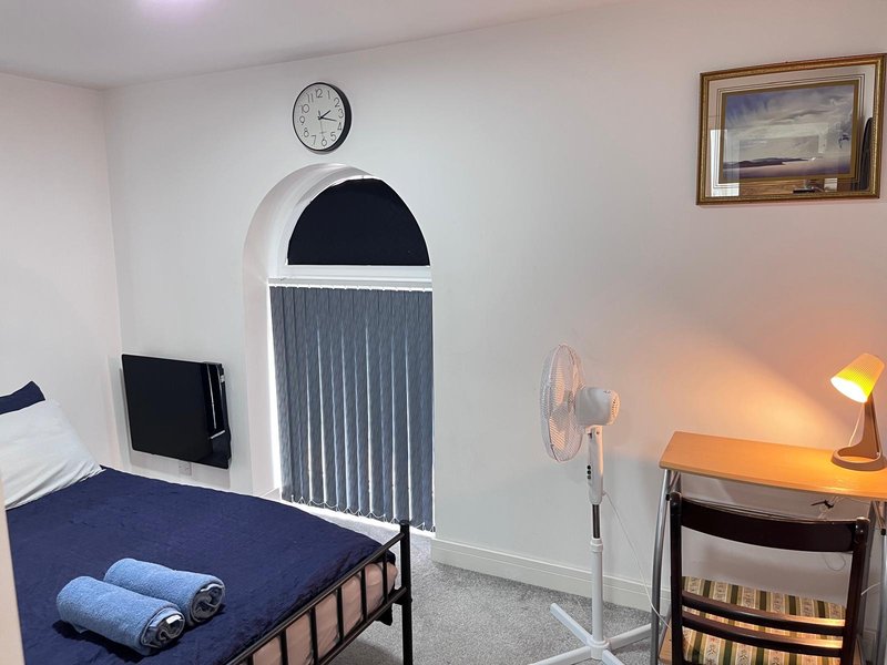 Bedroom with single bed, desk, clock, fan, and arched doorway with curtains