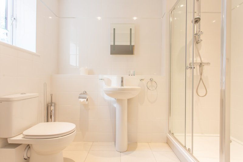 Clean modern bathroom with toilet, pedestal sink, shower enclosure and window
