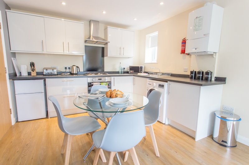 Modern kitchen with white cabinetry, dining table, and wooden flooring
