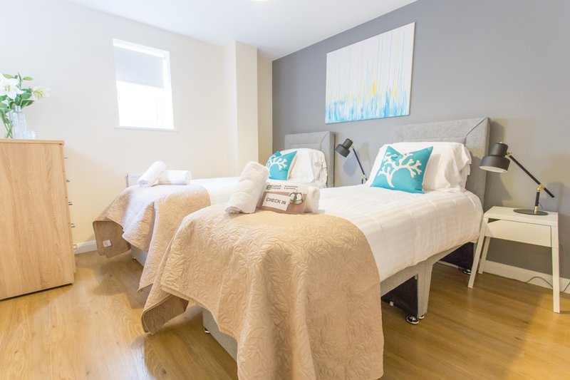 Bright bedroom with double bed, turquoise cushions, wooden wardrobe and hardwood flooring