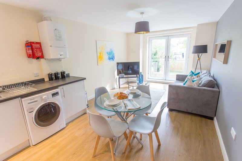 Open-plan living space with kitchen, dining table, sofa and glass doors to garden