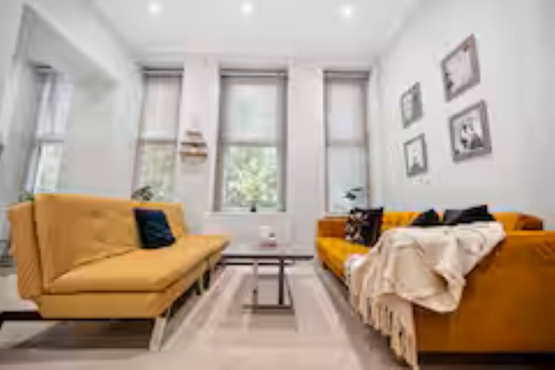 Bright living room with two yellow sofas, framed wall art, large windows and neutral flooring
