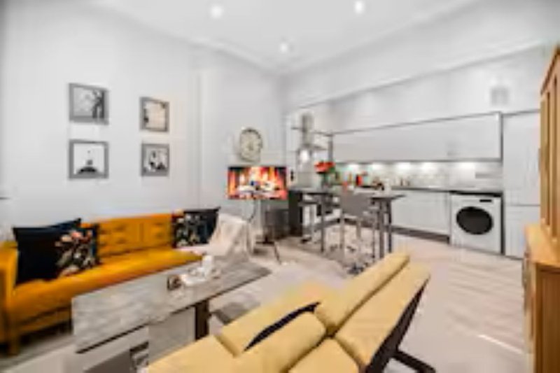Open-plan living and kitchen area with yellow sofa, dining table, and modern appliances