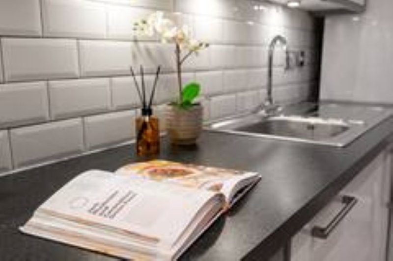 Modern kitchen with white subway tile backsplash, dark countertop, sink, flowers in vase, and magazine