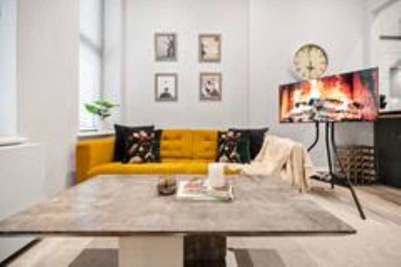 Modern living room with yellow sofa, fireplace display on TV, and dining table