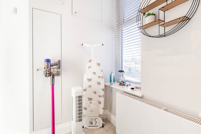 Compact laundry room with ironing board, vacuum cleaner, and wall-mounted mirror