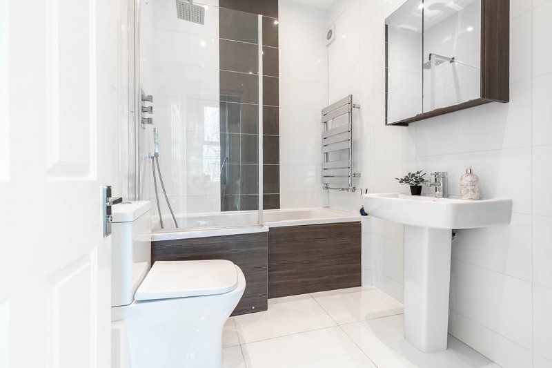 Modern bathroom with toilet, pedestal sink, bath with glass screen and mirror
