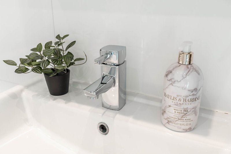 White bathroom sink with chrome faucet, potted plant, soap dispenser and toiletries