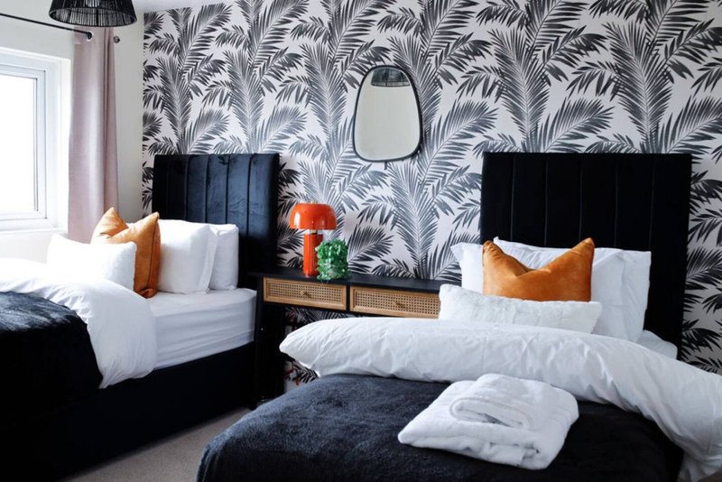 Twin bedroom with black upholstered beds, white bedding, orange cushions, and patterned wallpaper