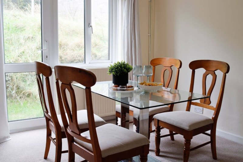 Dining room with glass table, four wooden chairs, large windows and garden view