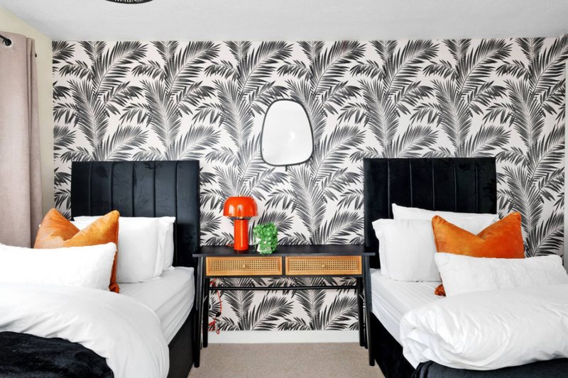 Twin bedroom with black headboards, white bedding, orange cushions and patterned wallpaper