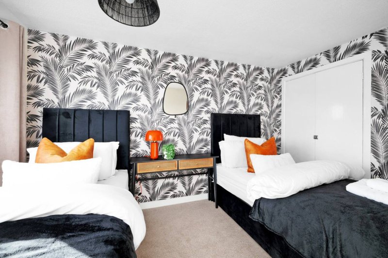 Twin bedroom with black headboards, white bedding, orange cushions, and palm-patterned wallpaper