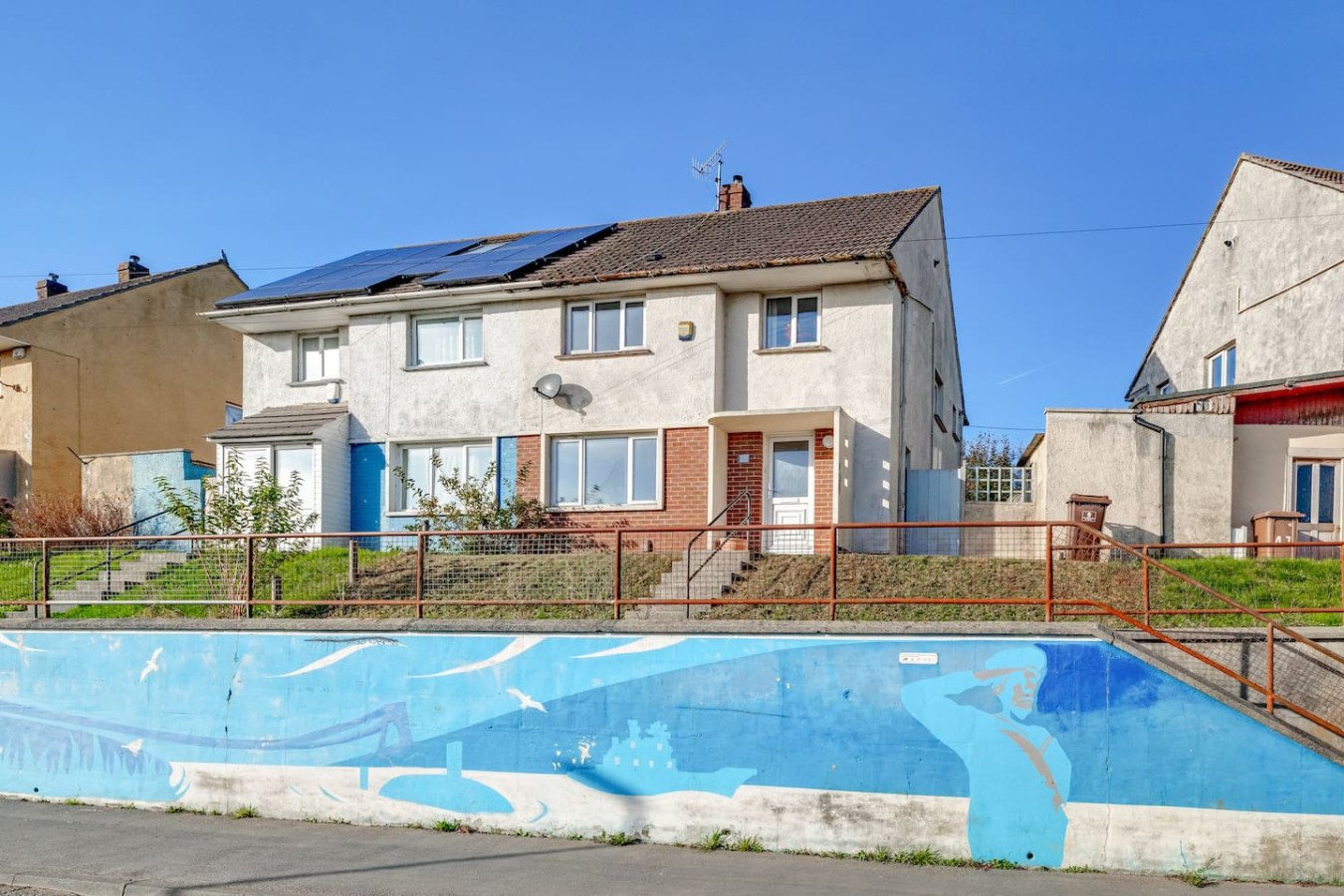 Semi-detached house with solar panels, garden fence and empty swimming pool in foreground