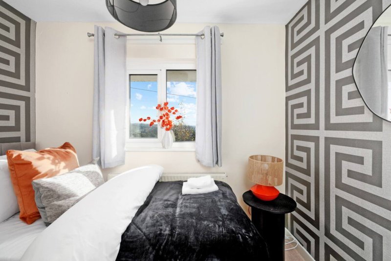 Modern bedroom with double bed, orange cushions, patterned wallpaper and window view