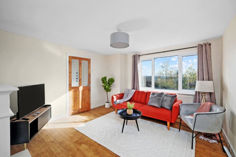Bright living room with red sofa, grey armchair, TV, wooden door and large windows