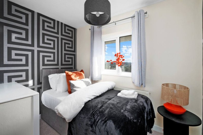 Modern bedroom with double bed, geometric headboard, black throws, and bright window view