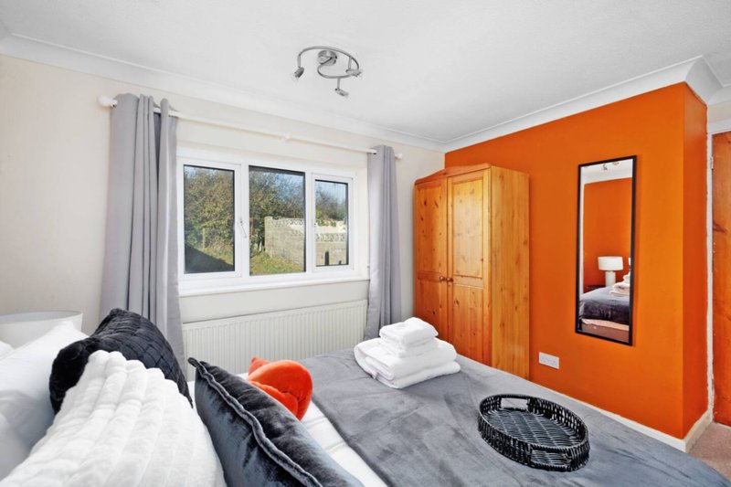 Bright bedroom with twin beds, orange accent wall, wooden wardrobe and garden views