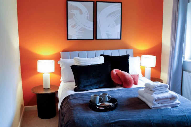 Bedroom with orange accent wall, double bed, black and pink cushions, bedside lamps