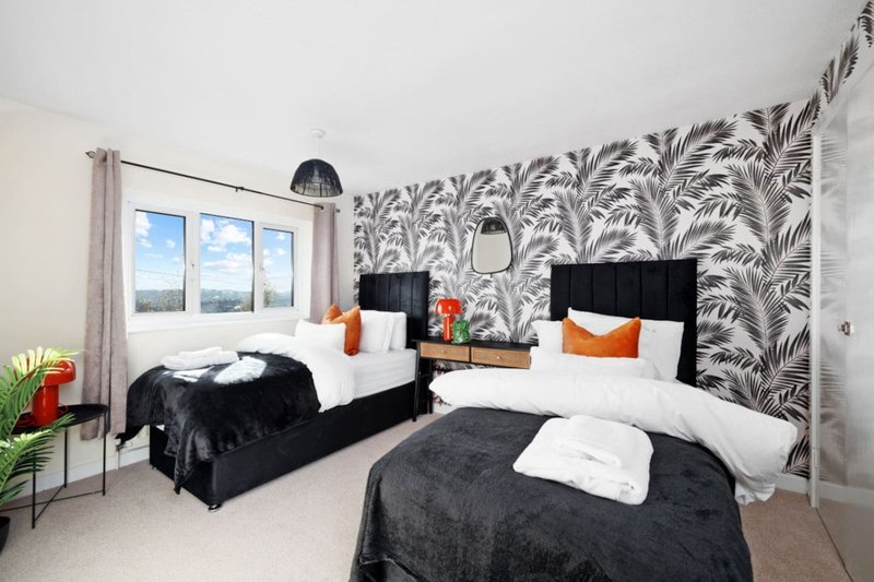 Bedroom with two beds, black headboards, white bedding, patterned wallpaper, and windows