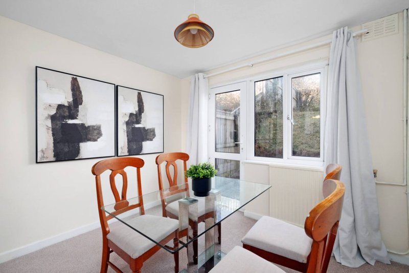Dining room with glass table, wooden chairs, wall art, and garden views through windows