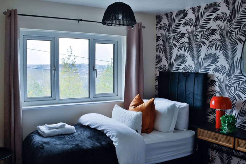 Modern bedroom with double bed, patterned wallpaper, large window with countryside view
