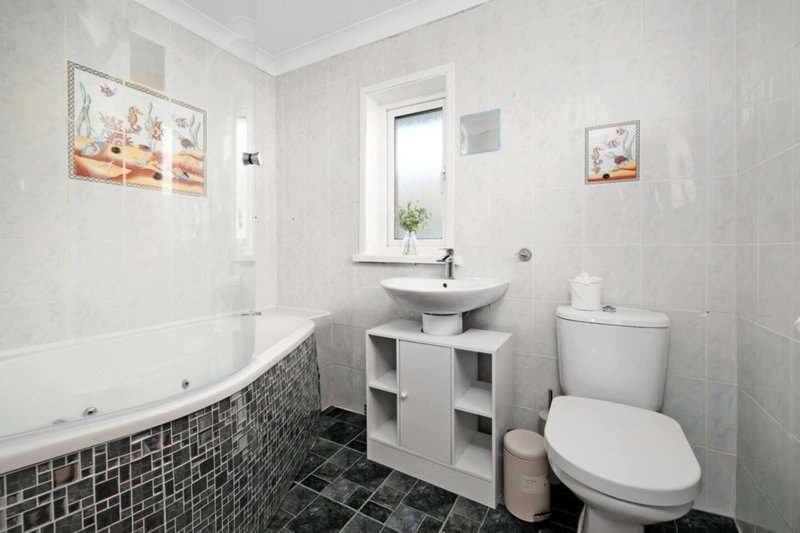 Modern bathroom with bathtub, sink vanity, toilet, and window with plant