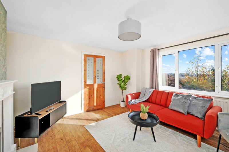 Bright living room with red sofa, wooden TV unit, black side table and large windows overlooking garden