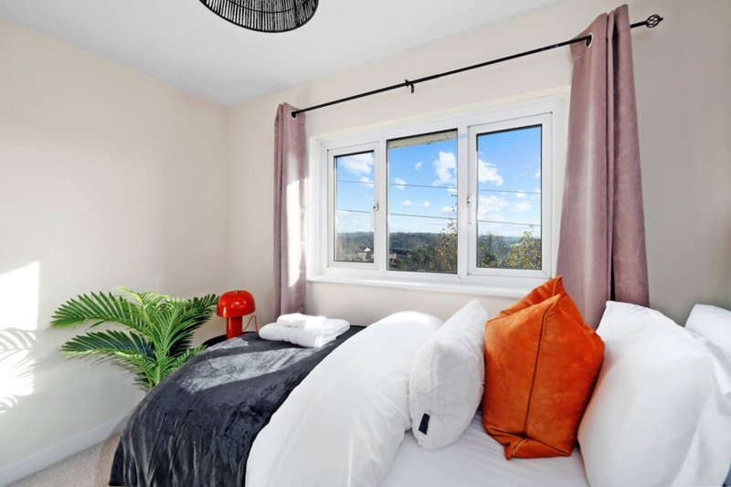 Bright bedroom with double bed, white pillows, orange cushions and countryside view from window