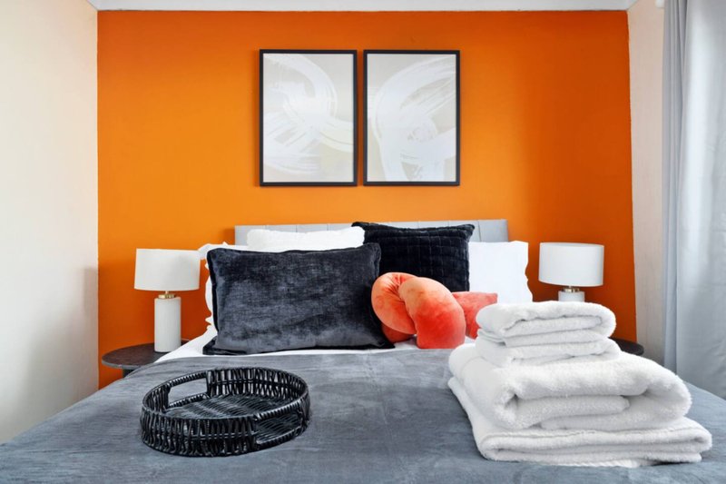 Bedroom with orange accent wall, double bed, dark cushions and white towels on mattress