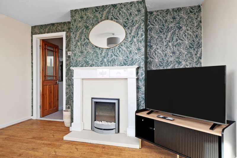 Living room with fireplace, TV on stand, patterned wallpaper and wooden floor