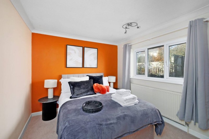 Bright bedroom with bold orange accent wall, double bed, white bedside tables and garden view windows