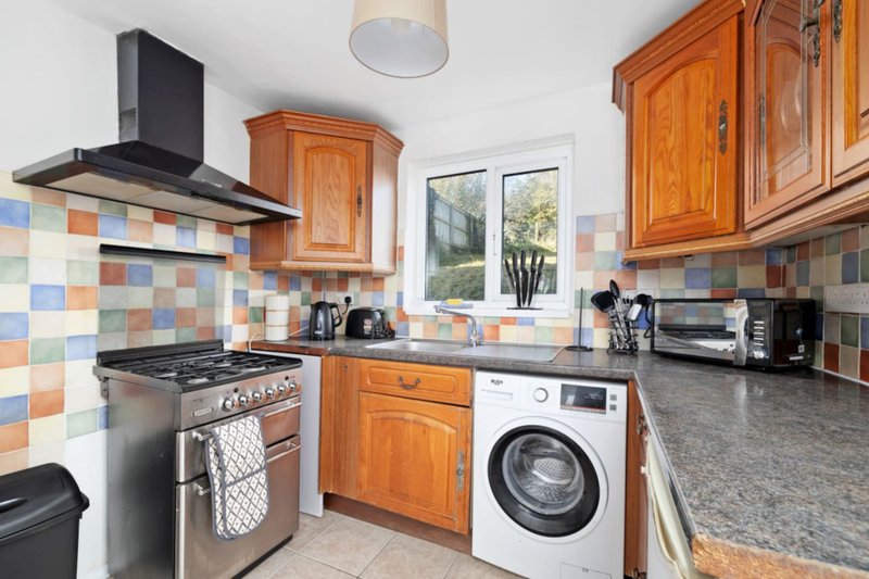 Kitchen with wooden cabinets, colorful tile backsplash, gas range and washing machine