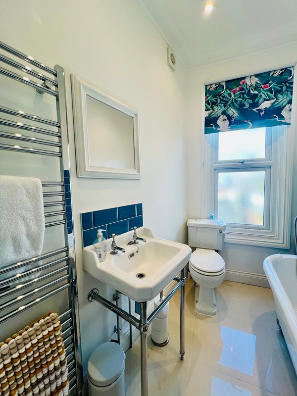 Bright bathroom with pedestal sink, toilet, heated towel rail and window