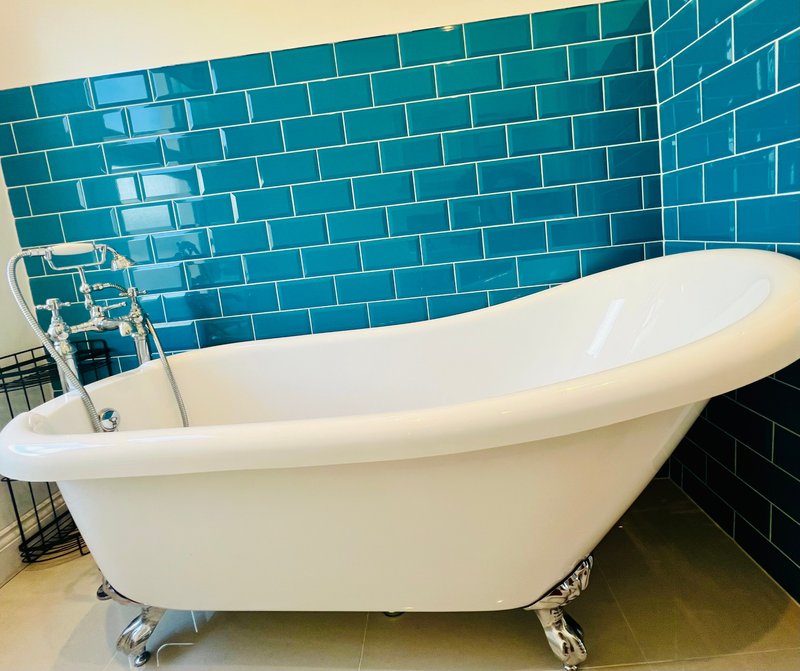 Modern bathroom with freestanding white bathtub and teal subway tile walls