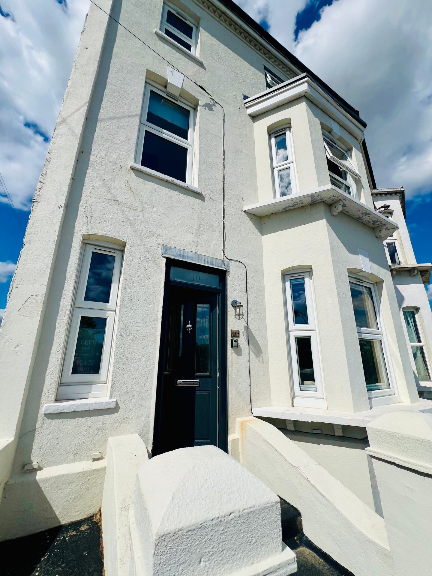 White rendered townhouse exterior with black door, multiple windows and blue sky