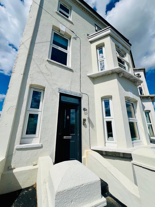 White rendered townhouse exterior with black door, multiple windows and blue sky
