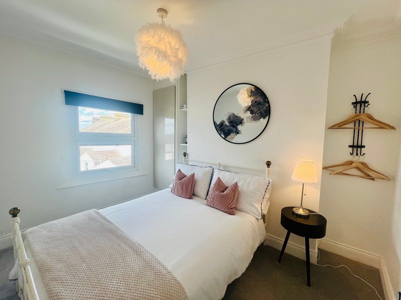 Bright modern bedroom with double bed, pendant light, circular wall art and wooden coat hangers
