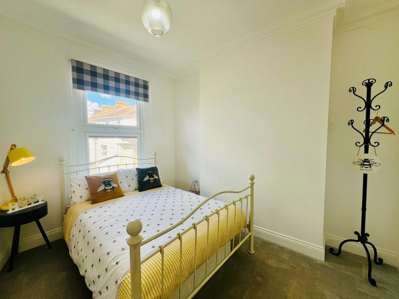 Bright bedroom with single brass bed, checkered window blind, yellow bedside lamp and coat stand