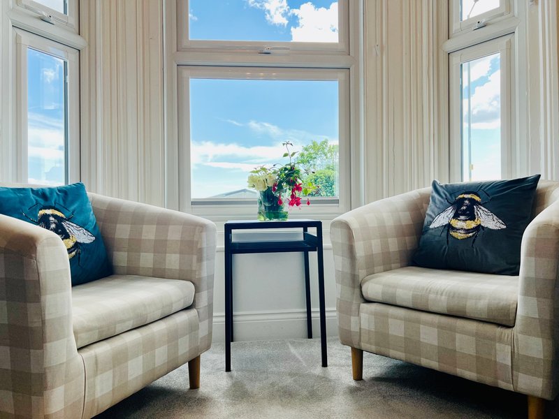 Bright seating area with two upholstered armchairs, small black table, and large windows overlooking water