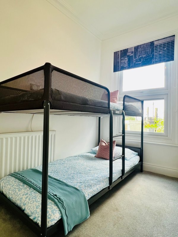 Bedroom with black metal bunk beds, green bedding, window with blue blind and radiator