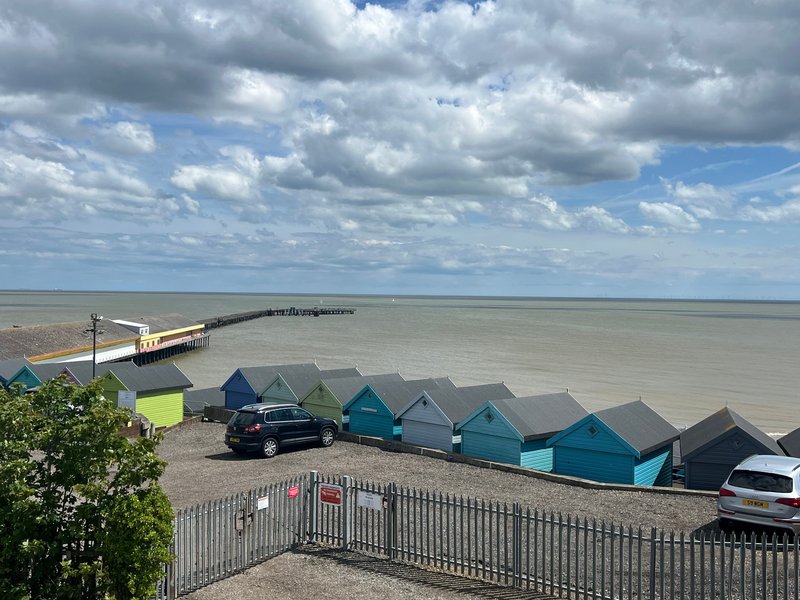 Coastal property view with beach huts, pier, parked cars and sea horizon