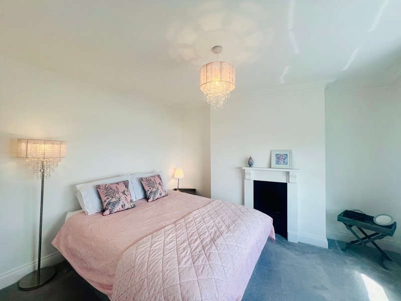 Bedroom with pink bedding, decorative pillows, floor lamp, pendant light and fireplace