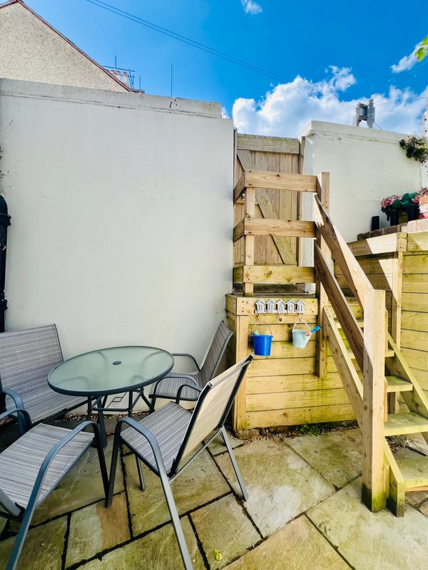 Compact paved courtyard with outdoor seating table, chairs, and wooden deck stairs