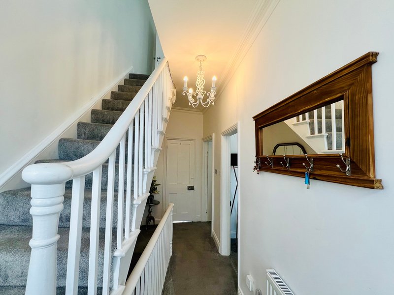 Hallway with staircase, white bannister, wooden framed mirror, and chandelier overhead
