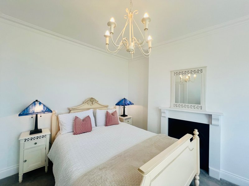 Bright bedroom with cream bed, blue table lamps, chandelier, fireplace and mirror