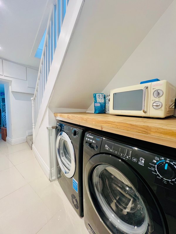 Utility room with two washing machines, wooden countertop, cream microwave and blue kitchen items